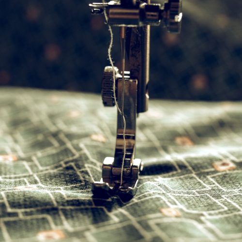 Primer plano de aguja de máquina de coser trabajando sobre tela verde